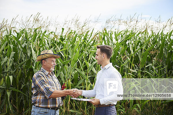 Farmer and businessman shaking hands at the cornfield