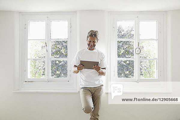 Mature man standing at window using digital tablet