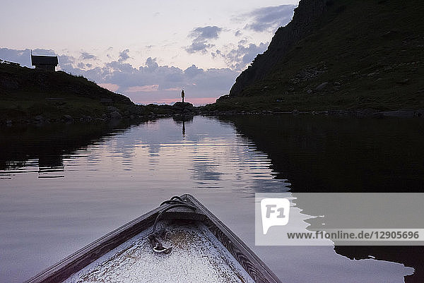 Austria  Tyrol  Fieberbrunn  Wildseeloder  bow of a boat on lake Wildsee with person standing at lakeshore at dusk