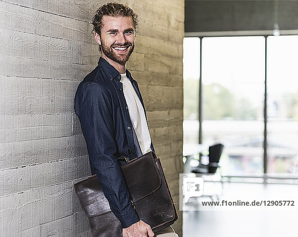 Smiling casual businessman standing on office floor holding briefcase