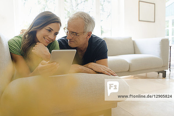 Smiling mature couple lying on couch at home sharing tablet