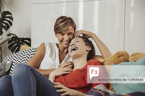 Happy lesbian couple laughing and cuddling on couch