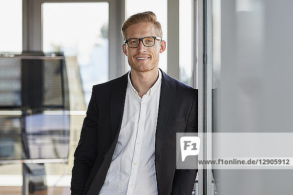 Portrait of smiling businessman in office leaning against window