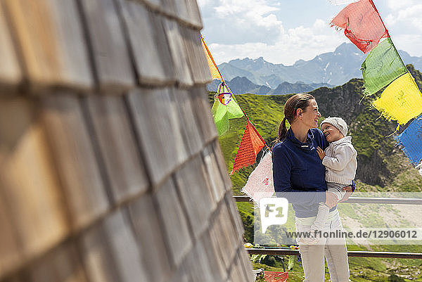Germany  Bavaria  Oberstdorf  happy mother carrying little daughter on a mountain hut surrounded by pennants