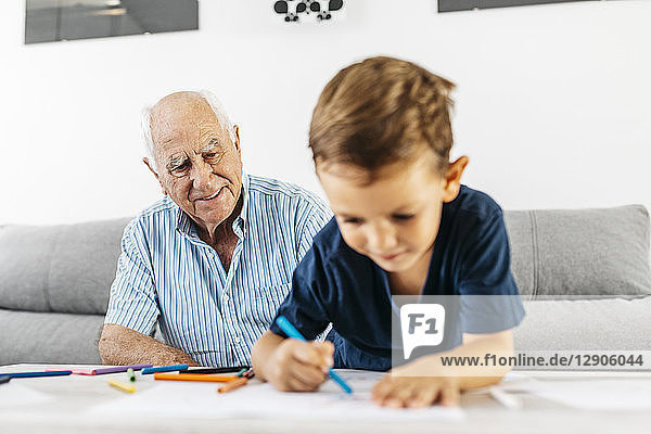 Portrait of smiling grandfather watching his grandson drawing with coloured pencils