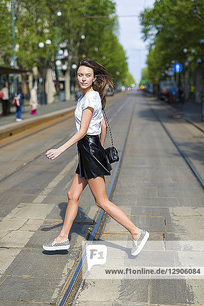 Young woman crossing a street with tramway tracks in the city