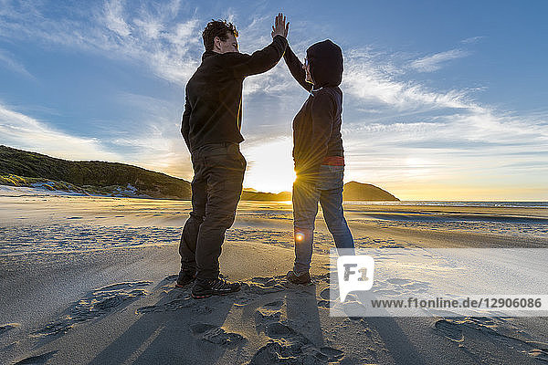 New Zealand  South Island  Puponga  Wharariki Beach  Couple high fiving on the beach at sunset