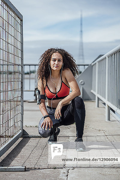 Portrait of young athletic woman with earbuds crouching outdoors