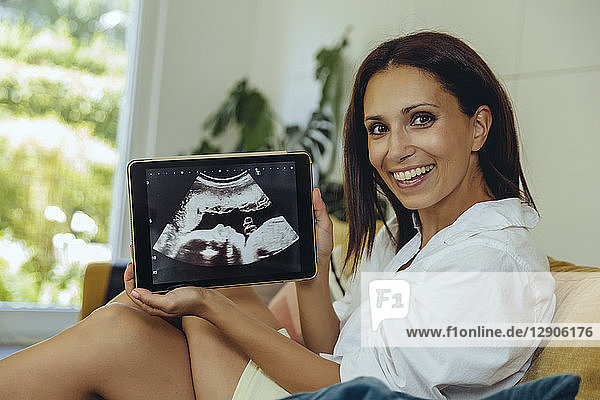 Portrait of smiling woman showing ultrasound picture of unborn child on couch