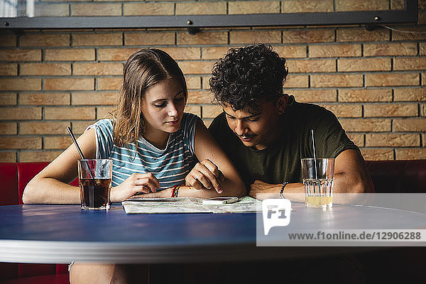Young couple sitting at table in a cafe with map and cell phone