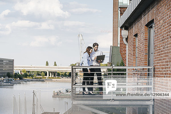 Business people standing on balcony  discussing  using laptop