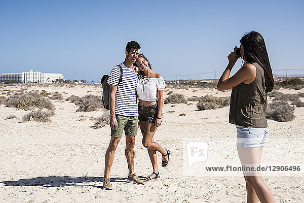 Young woman taking pictures of a young couple on the beach