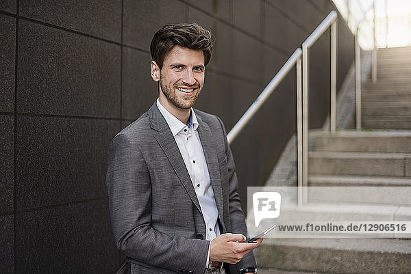 Portrait of smiling businessman with cell phone on stairs