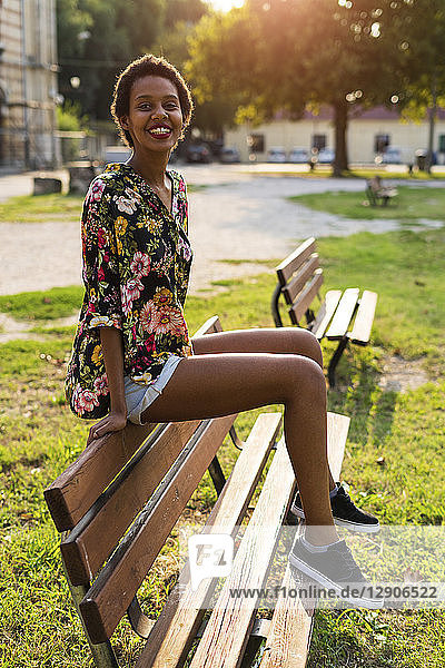 Portrait of smiling young woman sitting on bench in a park