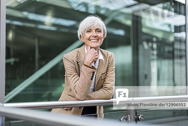Portrait of smiling senior businesswoman leaning on railing in the city