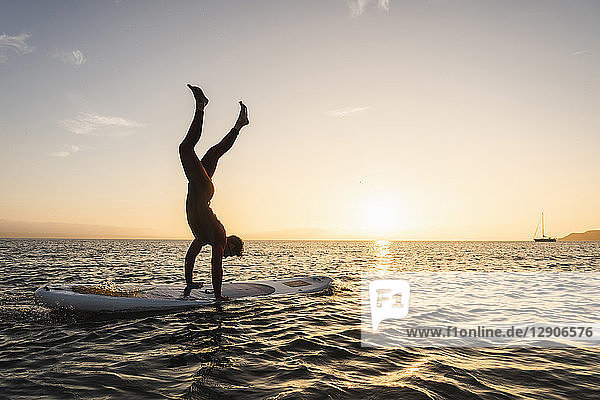 Young man doing handstand on paddleboard at sunset