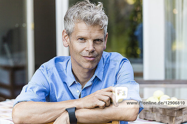 Portrait of smiling mature man with grey hair sitting on terrace