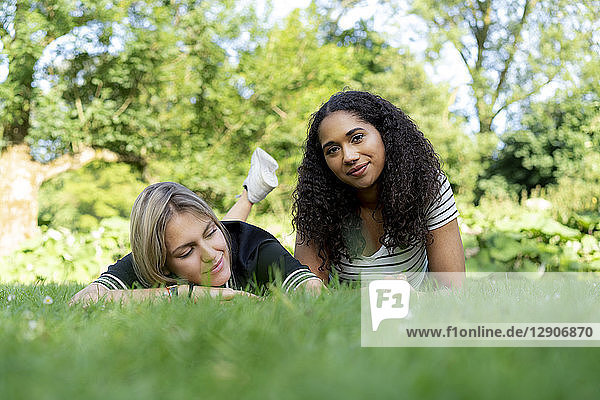 Two girlfriends relaxing in grass in a park