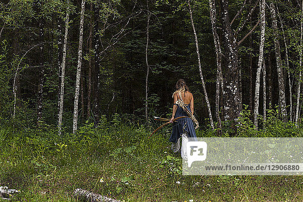 Rear view of woman walking in a forest with bow and arrow