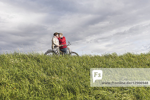 Senior couple with bicycles kissing in rural landscape under cloudy sky