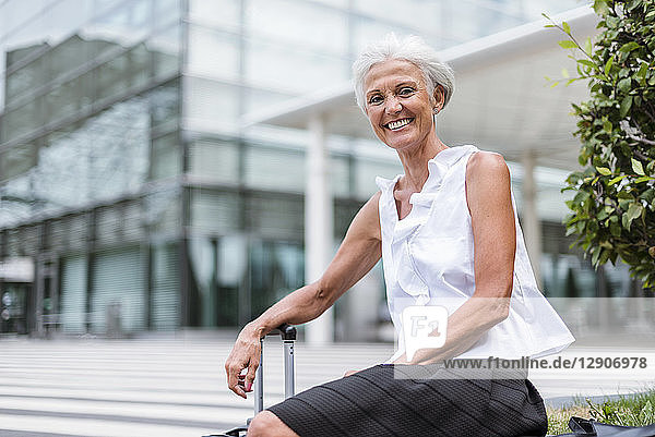 Portrait of happy senior woman with baggage sitting in the city