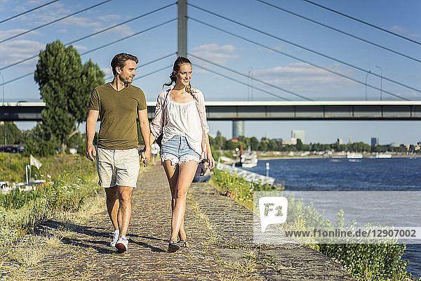 Happy couple walking hand in hand on waterfront promenade in summer
