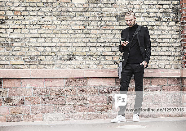 Young man standing at brick wall looking at cell phone