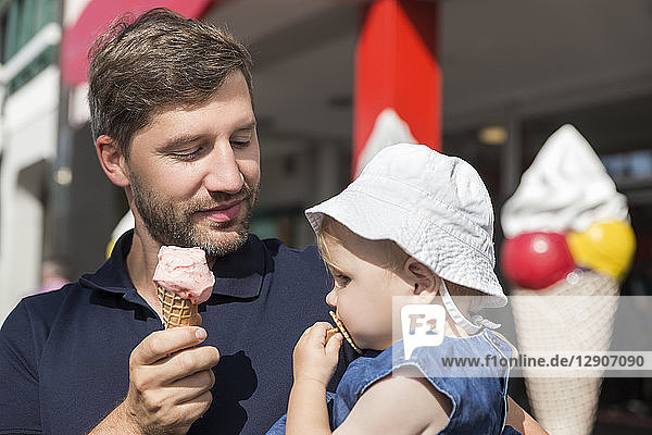 Father eating ice cream holding daughter