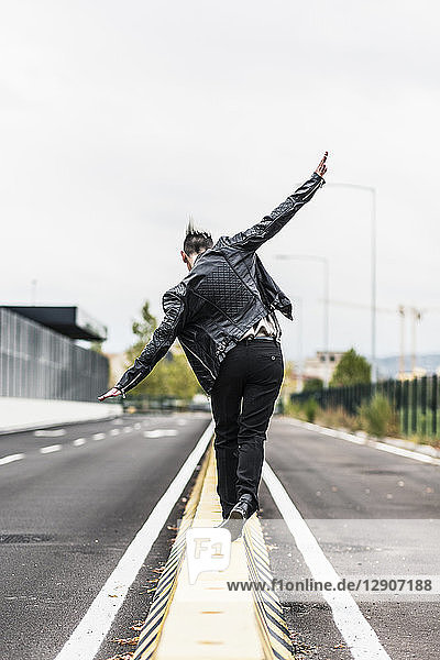 Rear view of punk woman balancing on a barrier at the roadside with outstretched arms
