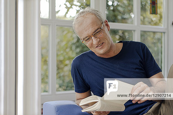 Smiling mature man at home reading book