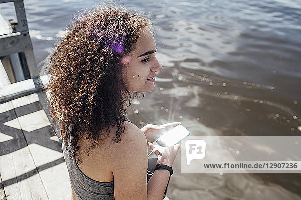 Smiling young athletic woman with smartphone at the riverside