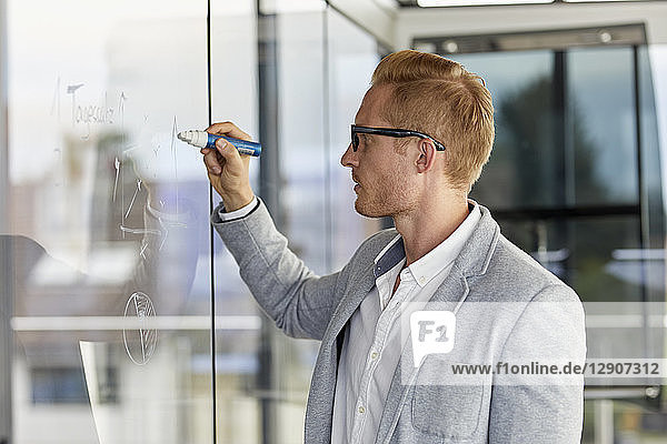 Businessman writing on glass pane in office