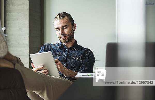 Businessman sitting in office with feet up using tablet