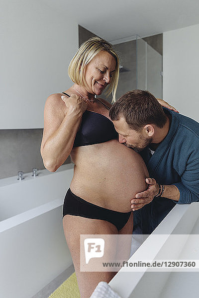 Mature husband kissing expectant mother?s belly in bathroom