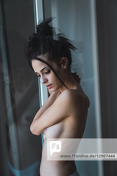 Beautiful barechested young woman standing at the window