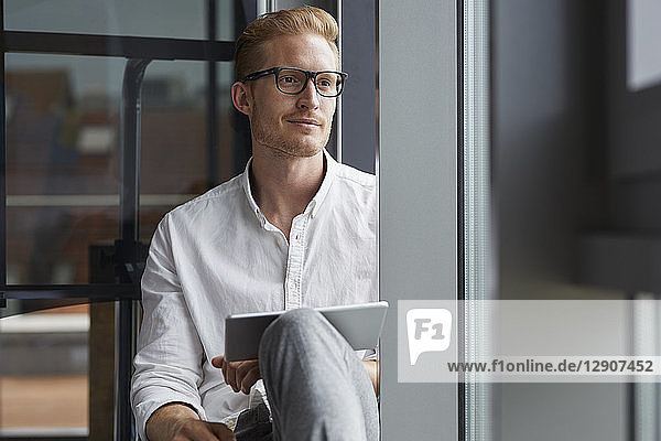 Smiling businessman sitting on windowsill with tablet