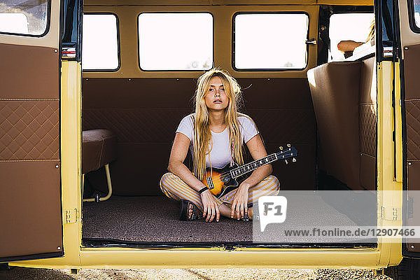 Young woman sitting in a van with a guitar