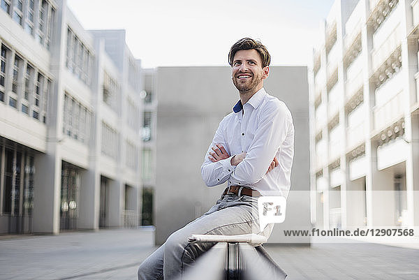 Smiling businessman sitting in the city looking around