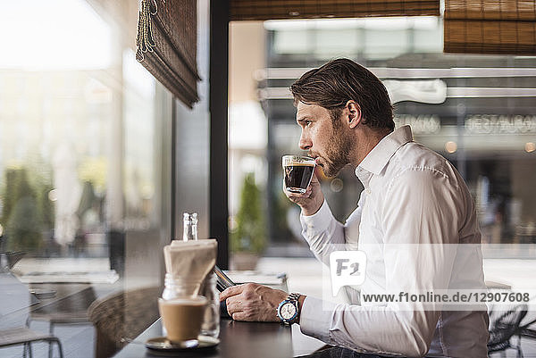 Businessman with tablet in a cafe drinking coffee from glass