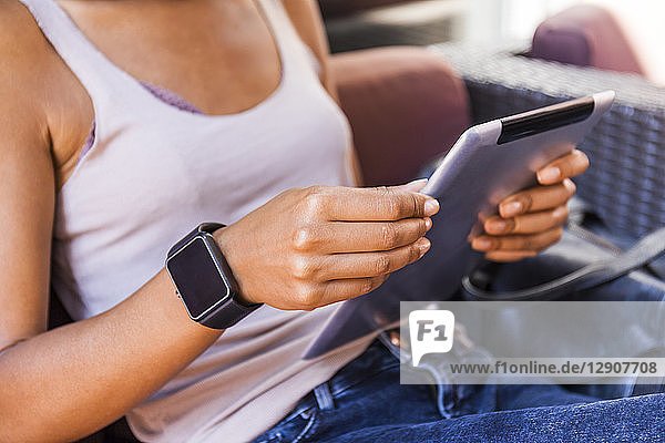 Young woman with smartwatch sitting at sidewalk cafe using digital tablet  close-up