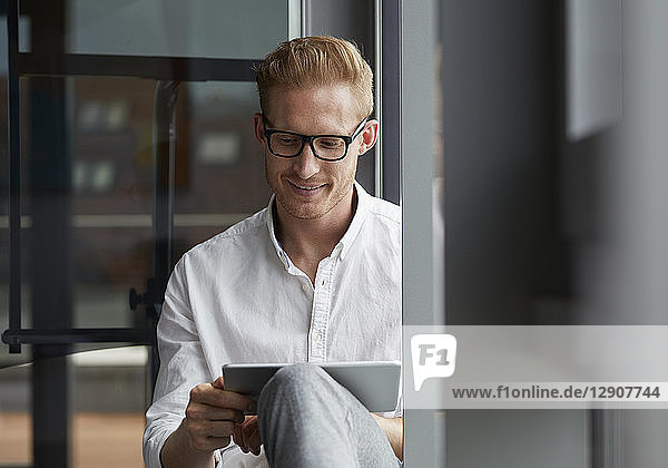 Smiling businessman sitting on windowsill using tablet