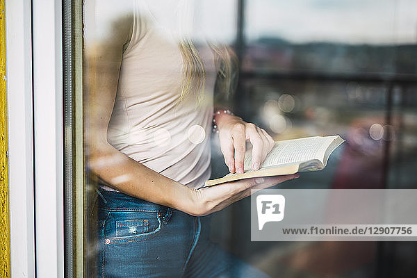 Close-up of young woman reading a book behind windowpane