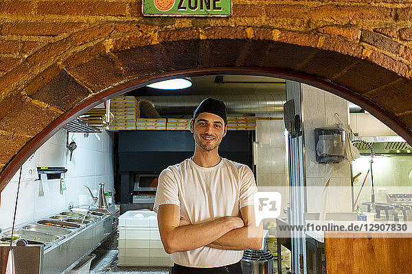 Portrait of confident pizza baker standing in kitchen
