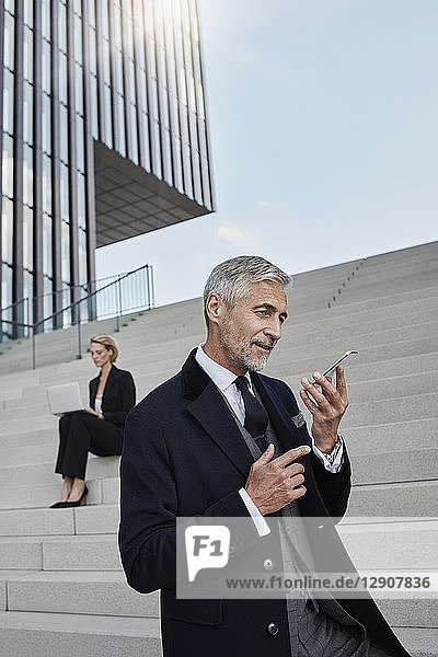 Portrait of businessman talking on the phone while business woman working on laptop in the background