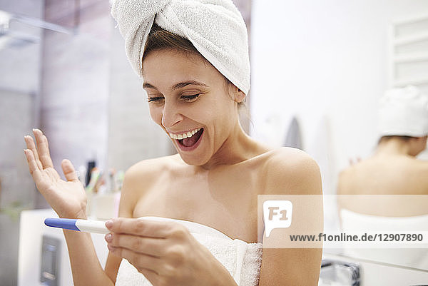 Portrait of excited young woman looking at pregnancy test in bathroom