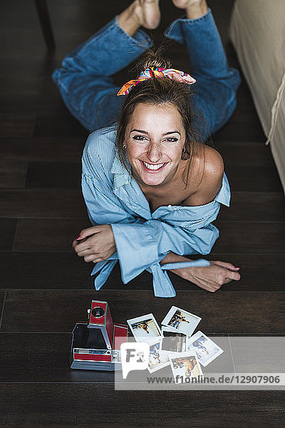 Portrait of happy young woman lying on the floor with instant photos of herself