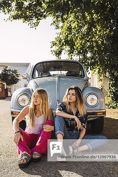 Two young women sitting outside at a vintage car