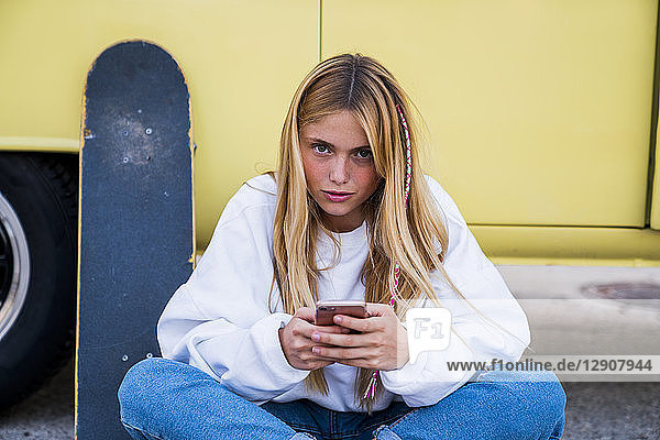 Young woman with skateboard and cell phone sitting at a van