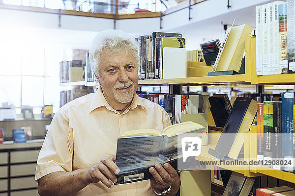 Portrait of senior man in a city library holding book