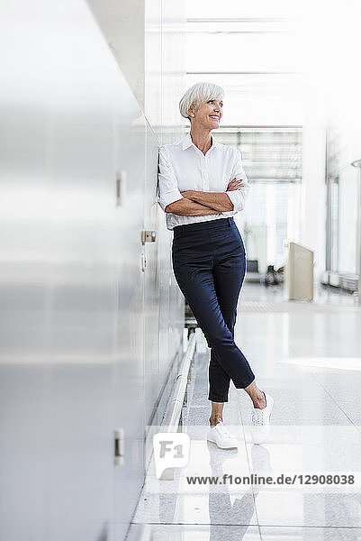 Smiling senior businesswoman leaning against a wall